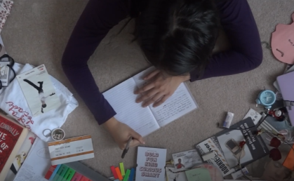 Flat overhead shot of me lying face-down on the carpet, writing in a notebook, surrounded by different trinkets